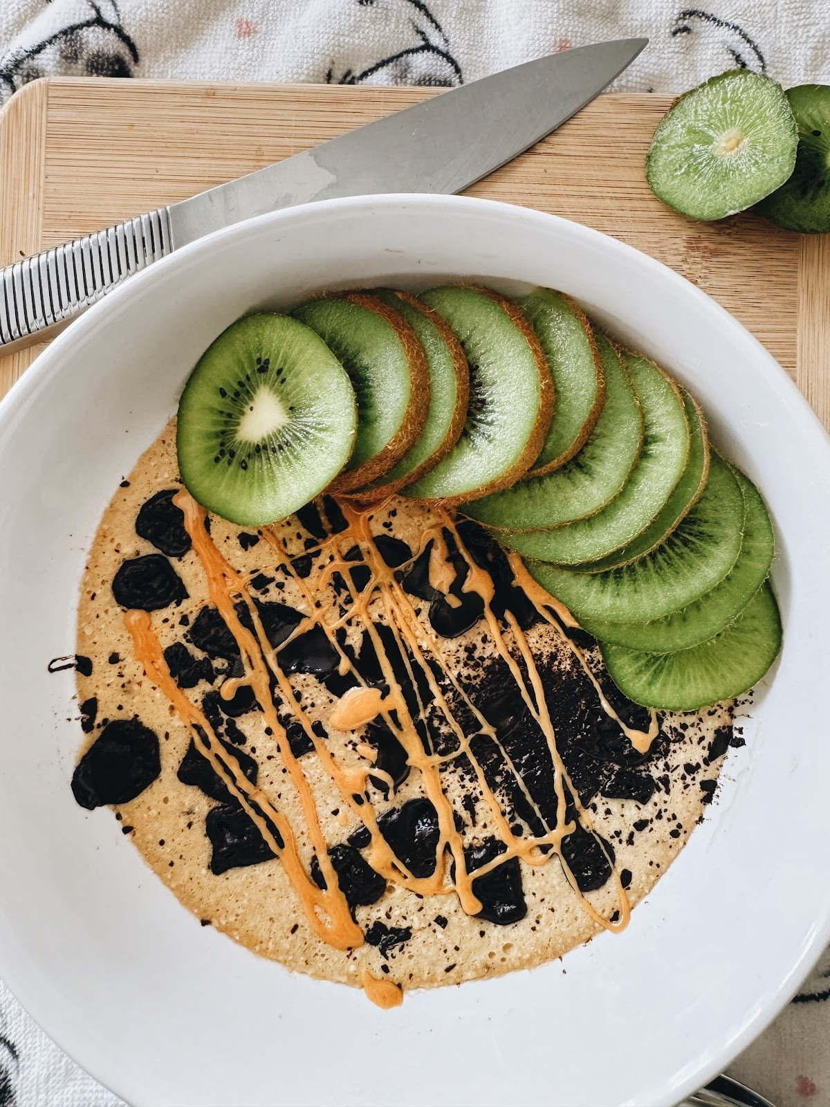 Blended Microwave Banana Oats in a bowl with Kiwi and peanut butter drizzle