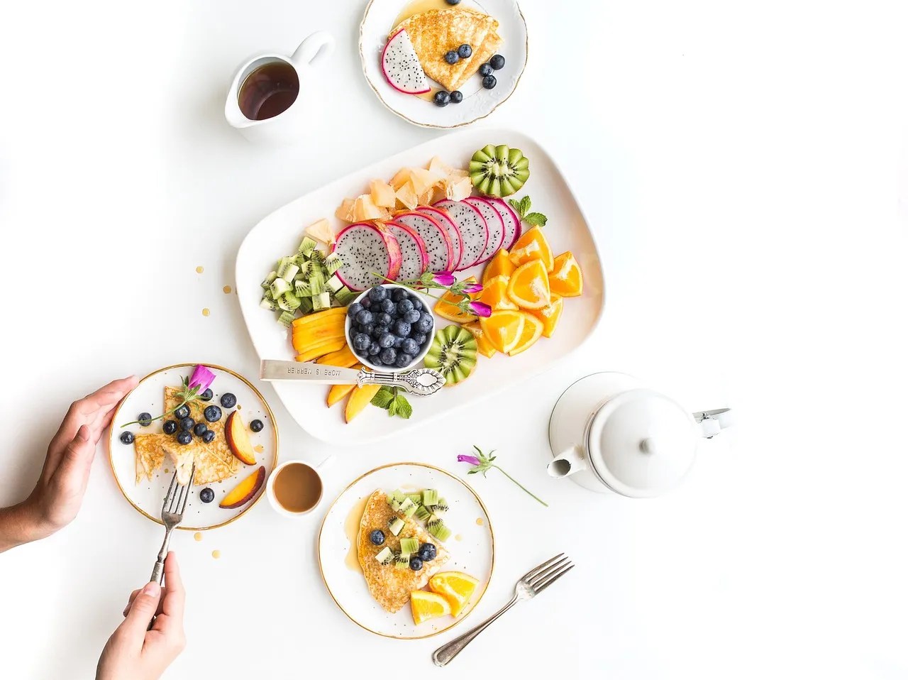 Healthy breakfast with fresh fruits, crepes, and tea on a white table for a balanced weight loss routine