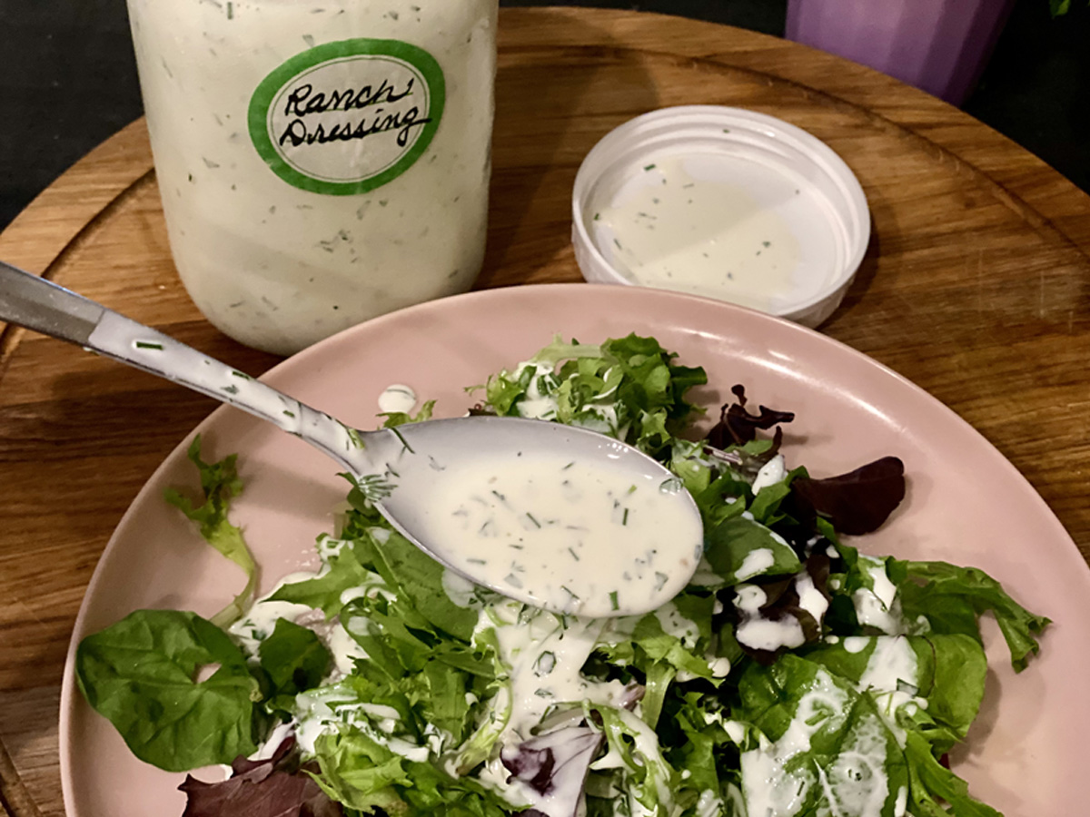 Large tablespoon of Homemade Dairy-Free Ranch Dressing (Whole30 compliant) drizzeled over mixed greens on a neutral plate.