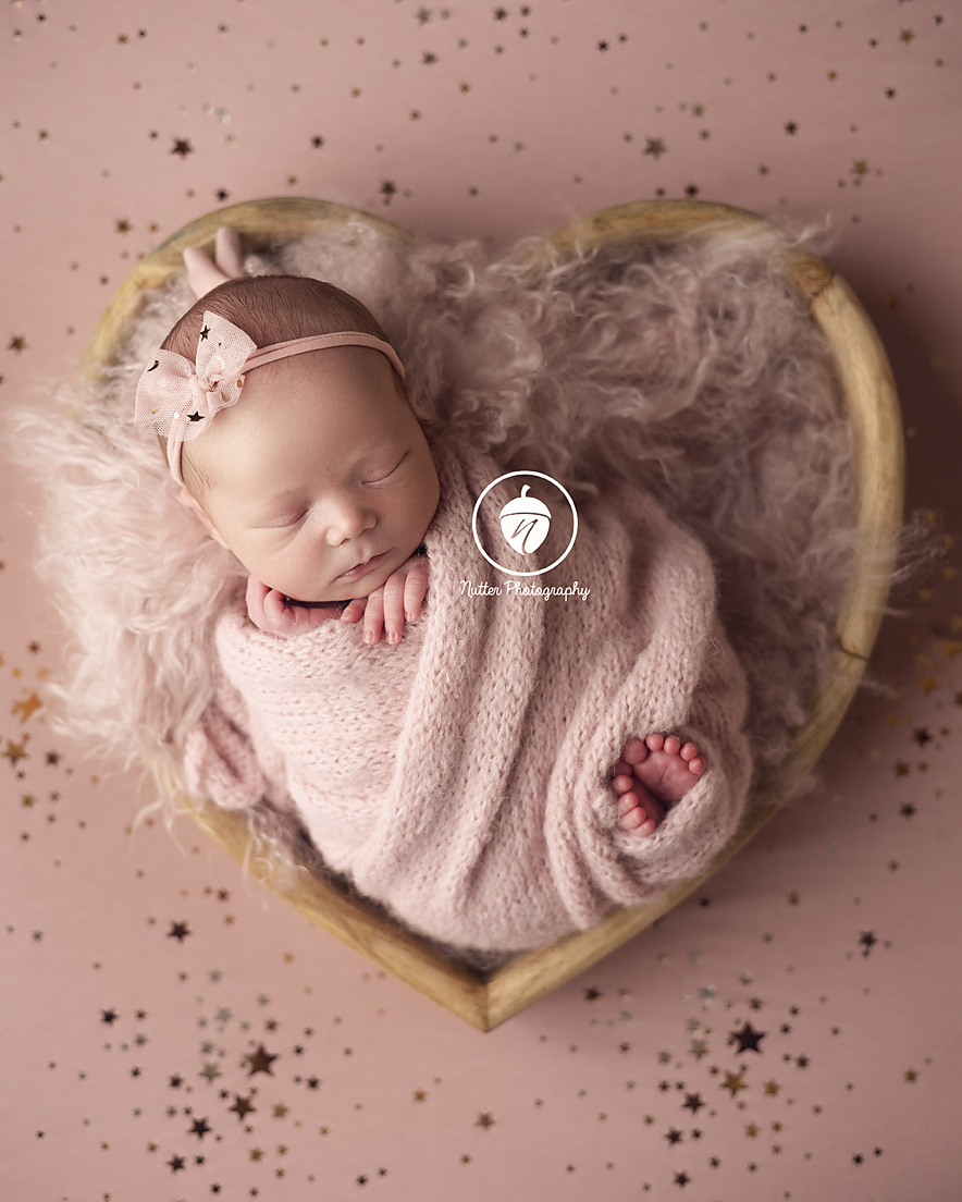 newborn baby girl in heart bowl on pink stars