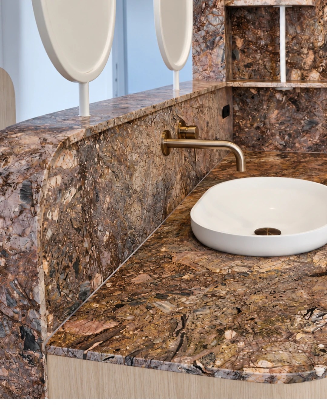 Richly patterned stone vanity and splashback with a white oval basin and brushed brass tap