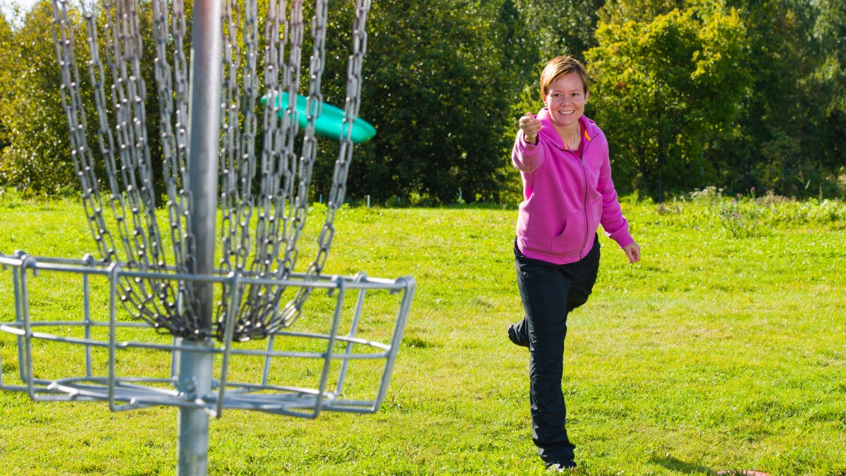 Woman throws a disc at a disc golf basket.