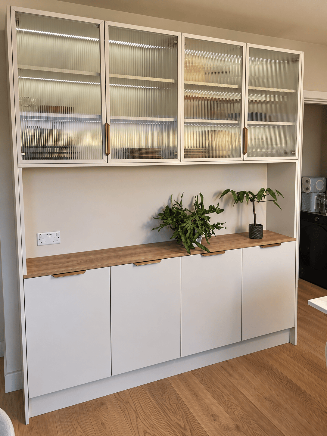 Bespoke white dresser with fluted glass cabinets and integrated LED lighting in a modern dining area.