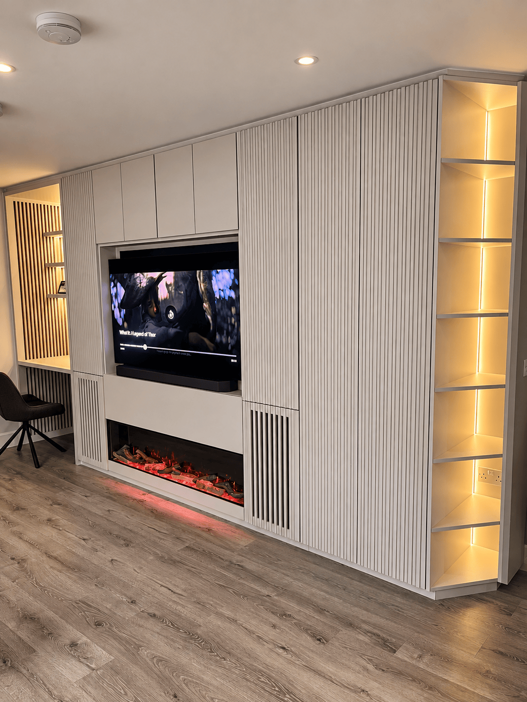 Bespoke living room TV wall unit with slatted doors, an integrated electric fireplace, and a built-in home office desk.