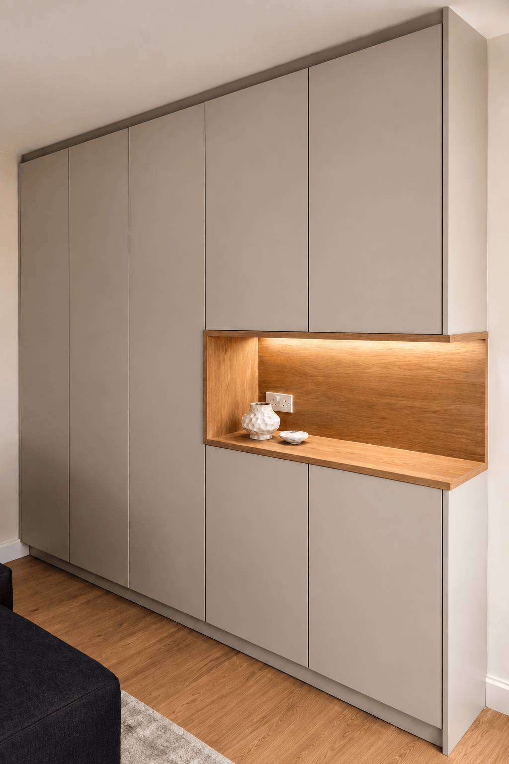 Floor-to-ceiling bespoke hallway wardrobe featuring handleless beige doors and an illuminated oak display niche.