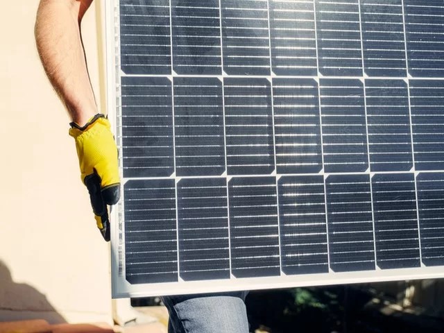 Personne avec des gants jaunes tenant un panneau solaire pour l'installer sur son fourgon