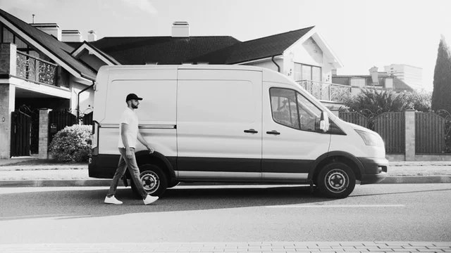 Homme passant devant son utilitaire aménagé blanc.