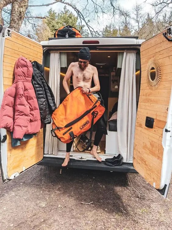 Vanlifer qui sort par l'arrière de son fourgon aménagé et qui range ses habits sur un porte-manteau