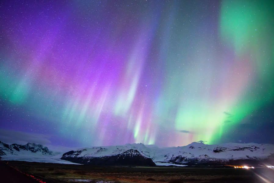 Purple and green aurora borealis over snow-capped mountains at night