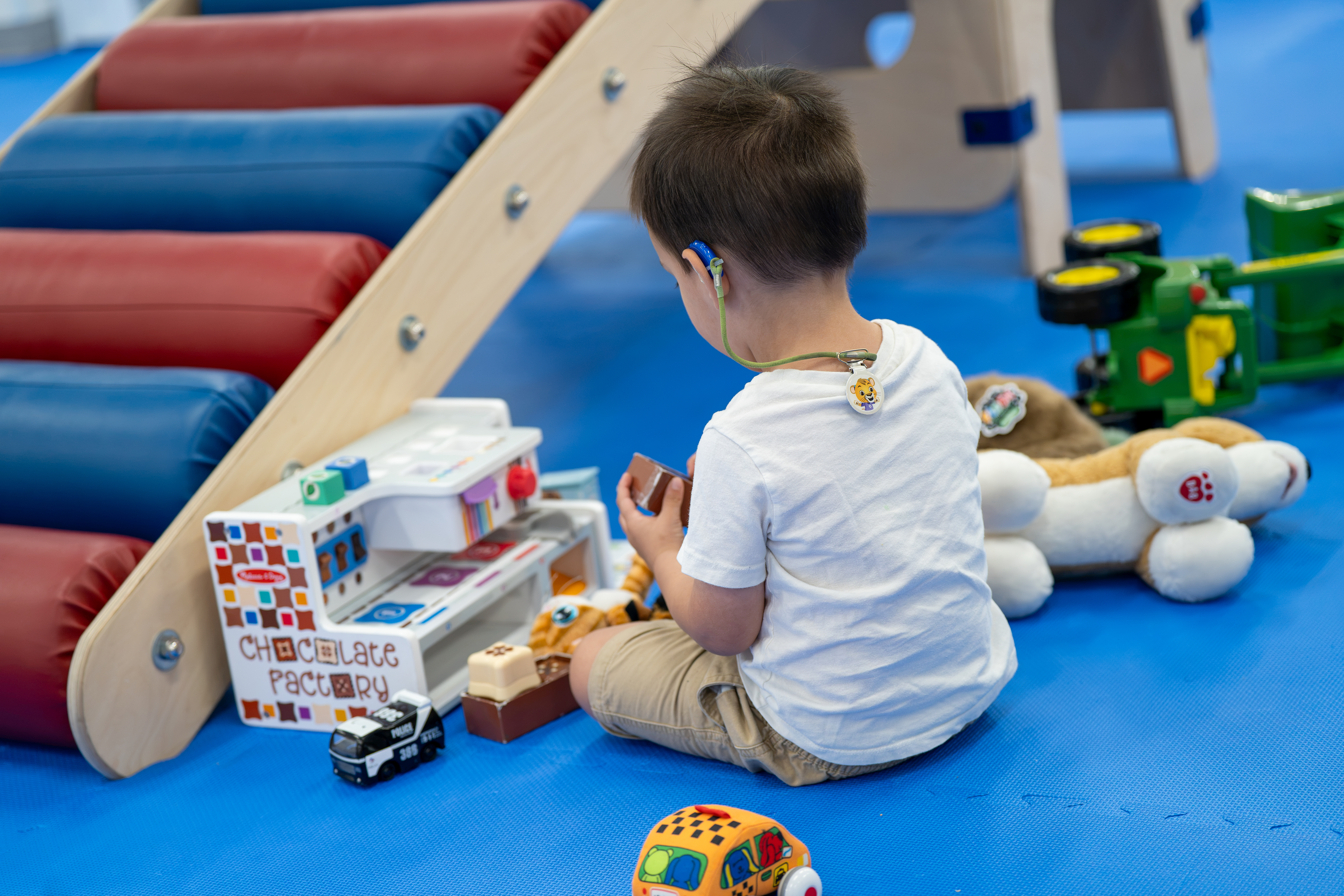 A child plays with toy vehicles beside the padded roller ramp.