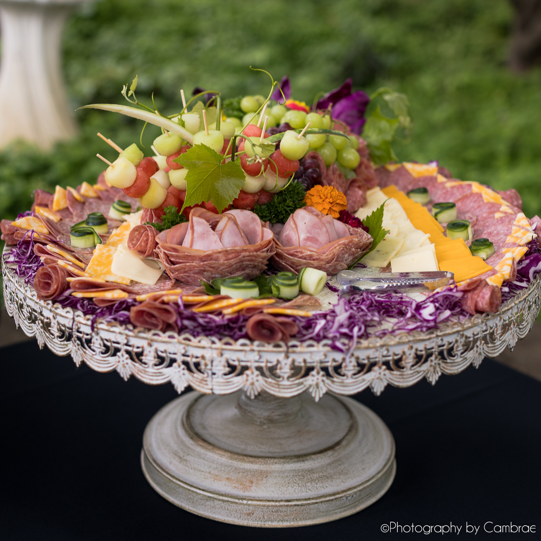 A charcuterie platter with sliced meat, cheese, grapes, and flowers