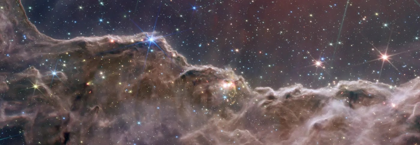 Infrared composite of the Cosmic Cliffs, a ridge of gas and dust beneath a field of stars in the Carina Nebula.