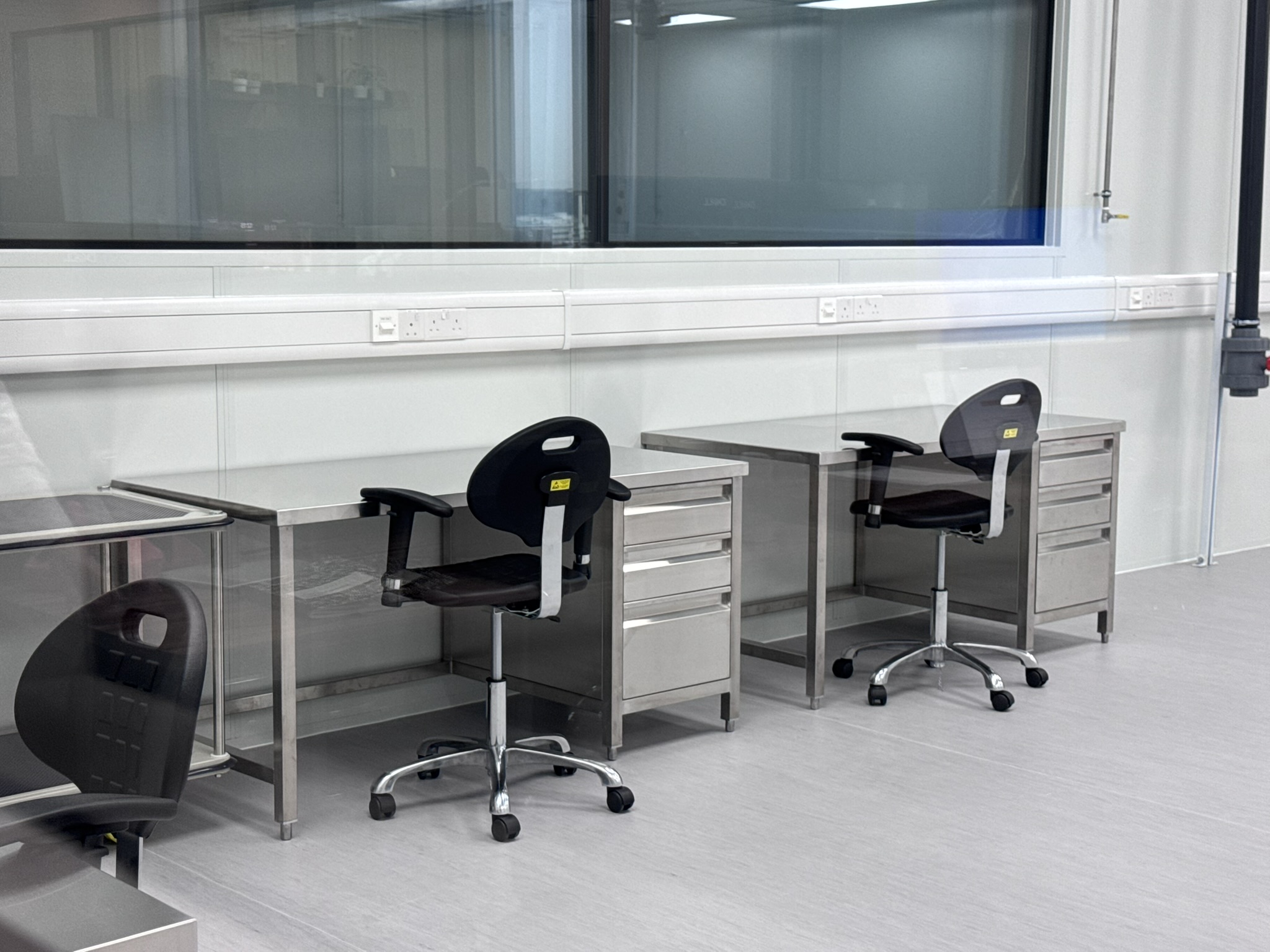 Stainless-steel cleanroom benches with drawer pedestals and ESD stools beside a glazed partition
