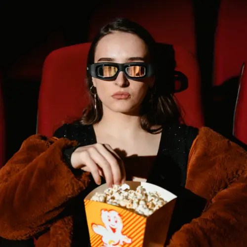 Woman enjoying popcorn in 3D movie theater, wearing 3D glasses.