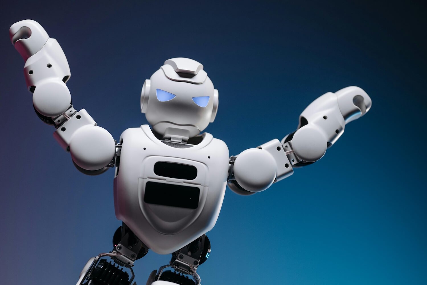 A white toy robot with its arms raised on a blue gradient background