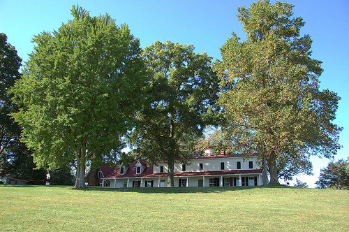 Historic red brick colonial manor house with large shade trees on manicured lawn