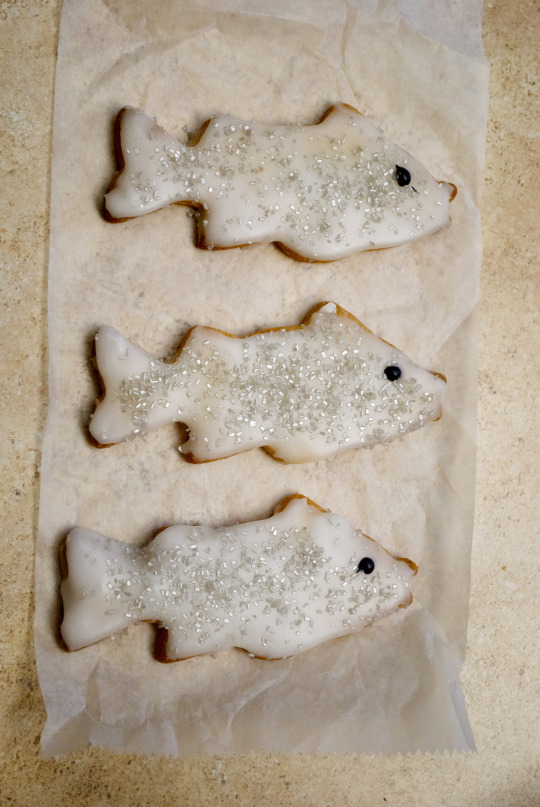 Three decorated fish-shaped cookies with white icing and silver sugar on parchment paper for Shadfest