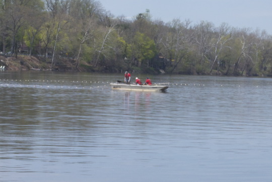 Small fishing boat on calm river with bare trees along shoreline during Shadfest