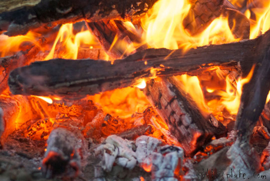 Glowing campfire coals and flames for outdoor Dutch oven cooking and slow-cooking beef à la mode over a campfire