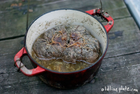 Large beef roast braised in red wine with vegetables in enameled Dutch oven on wooden deck