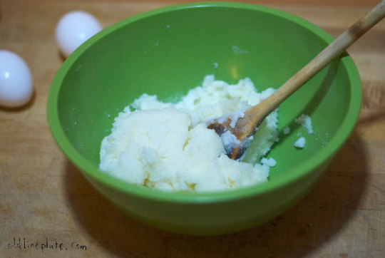 Green bowl with white cake batter and wooden spoon, eggs in background for vanilla butternut pound cake recipe