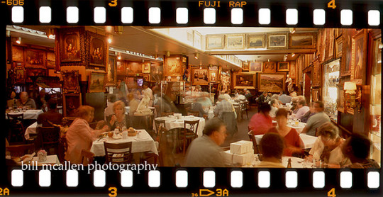 Cozy vintage restaurant dining room with patrons seated at tables, warm wood paneling and framed artwork on walls