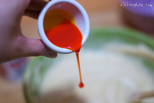 Bright red food flavoring dripping from white measuring cup onto vanilla butternut pound cake batter