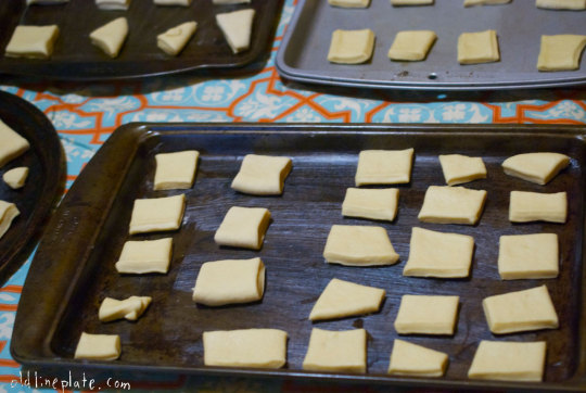 Unbaked fastnacht dough squares arranged on blue baking sheets to rise