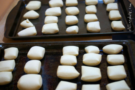 Two baking trays of risen fastnachts cooling on dark parchment paper, golden-brown pastries arranged in rows