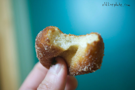 Close-up of a golden-brown fried fastnacht pastry dusted with powdered sugar, held in hand against blue background