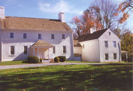 Historic colonial farmhouse with attached kitchen building, autumn foliage, white exterior, yellow door