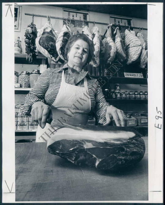 Woman in apron holding ham in butcher shop with hanging meats and jars