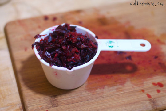 Shredded roasted beets in white measuring cup on wooden cutting board