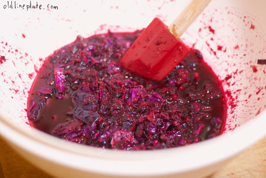 Homemade cabbage and beet relish being stirred in white bowl with red silicone spatula showing glossy texture