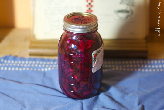 Mason jar filled with deep red beet relish on blue cloth with wooden background