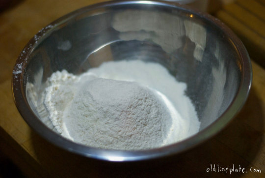 Dry ingredients for silver cake in metal bowl including flour and baking powder