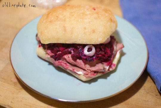 Beetroot relish and roast beef sandwich on a light blue plate with ciabatta and white onion ring garnish