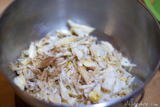 Shredded crab meat mixed with  seasonings in metal bowl for homemade crab cakes