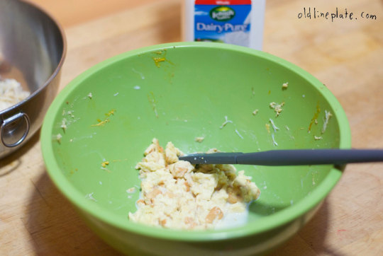 wetting crab cake ingredient bread in green bowl with black spoon, dairy products visible in background