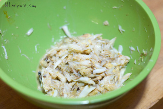 Shredded crab meat mixed with breadcrumbs and seasonings in green bowl for homemade crab cake preparation
