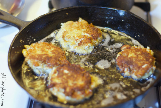 Golden-brown crab cakes frying in oil in a cast iron skillet, showing crispy exterior and classic Maryland preparation