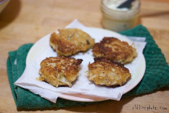 Golden-brown crab cakes on white plate with green napkin, crispy exterior, traditional Chesapeake Bay recipe