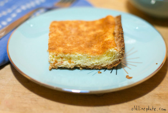 Golden-baked Smierkase cheesecake slice with creamy cottage cheese filling on light blue plate