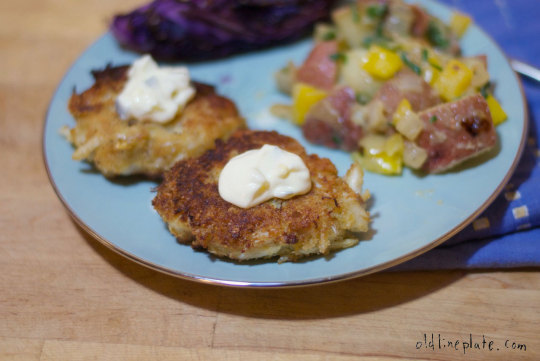 Golden-brown crab cakes with tartar sauce dollop served on blue plate with potato salad