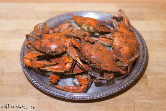 Plate of whole cooked crabs with reddish-brown shells served on a decorative gray platter on wooden surface