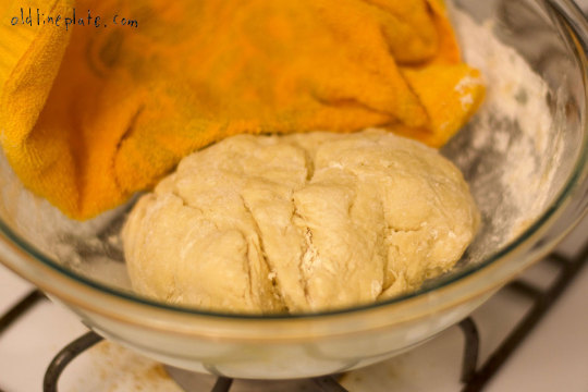 Dough for Baltimore peach cake rising in glass bowl covered with yellow towel