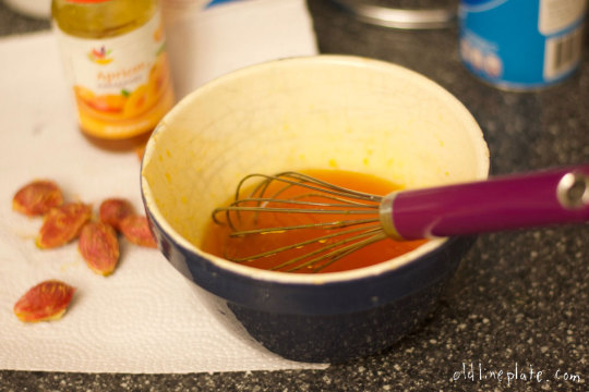 Whisking apricot jam together in bowl for Baltimore peach cake glaze with fresh peach pits nearby
