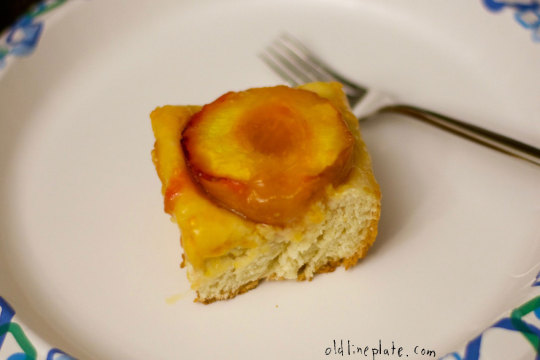 Close-up of a slice of Baltimore peach cake with glazed peach topping on a white plate with fork
