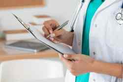 Close-up view of female doctor hands filling patient registration form.