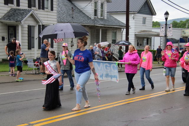(Rick MIller/Olean Star) USA National Miss New York State Sophia Babb of Allegany waves flag as she marches in the Allegany Memorial Day Parade as her mother, Brittany, holds an umbrella. Members of Enchanted Mountains Garden Club follow her.
